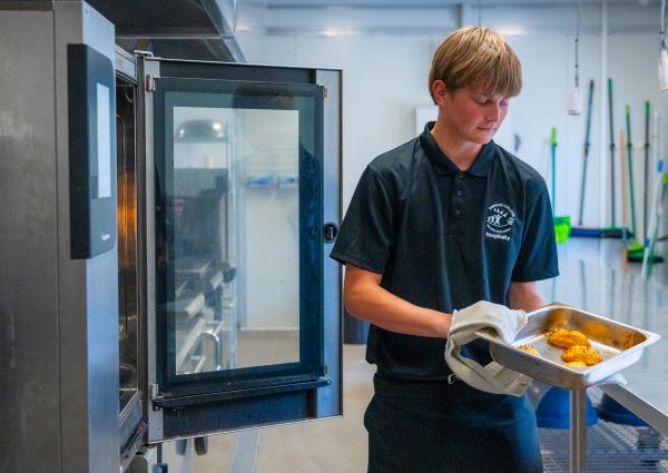 Hospitality student pulling roast potatoes out of a commercial oven using gloves