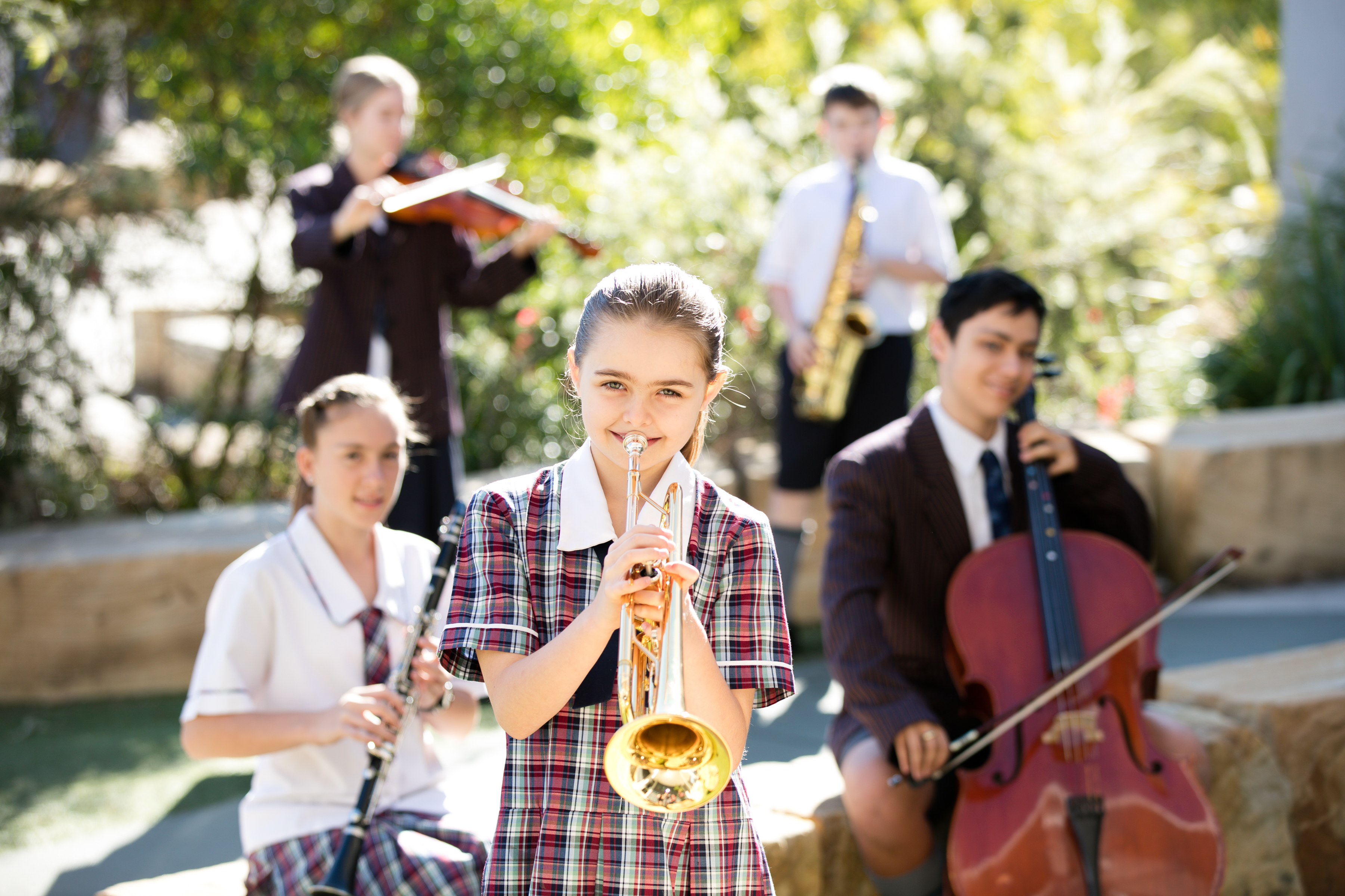 Students performing as part of a school music ensemble with trumpet, violin, clarinet, saxophone and cello outdoors