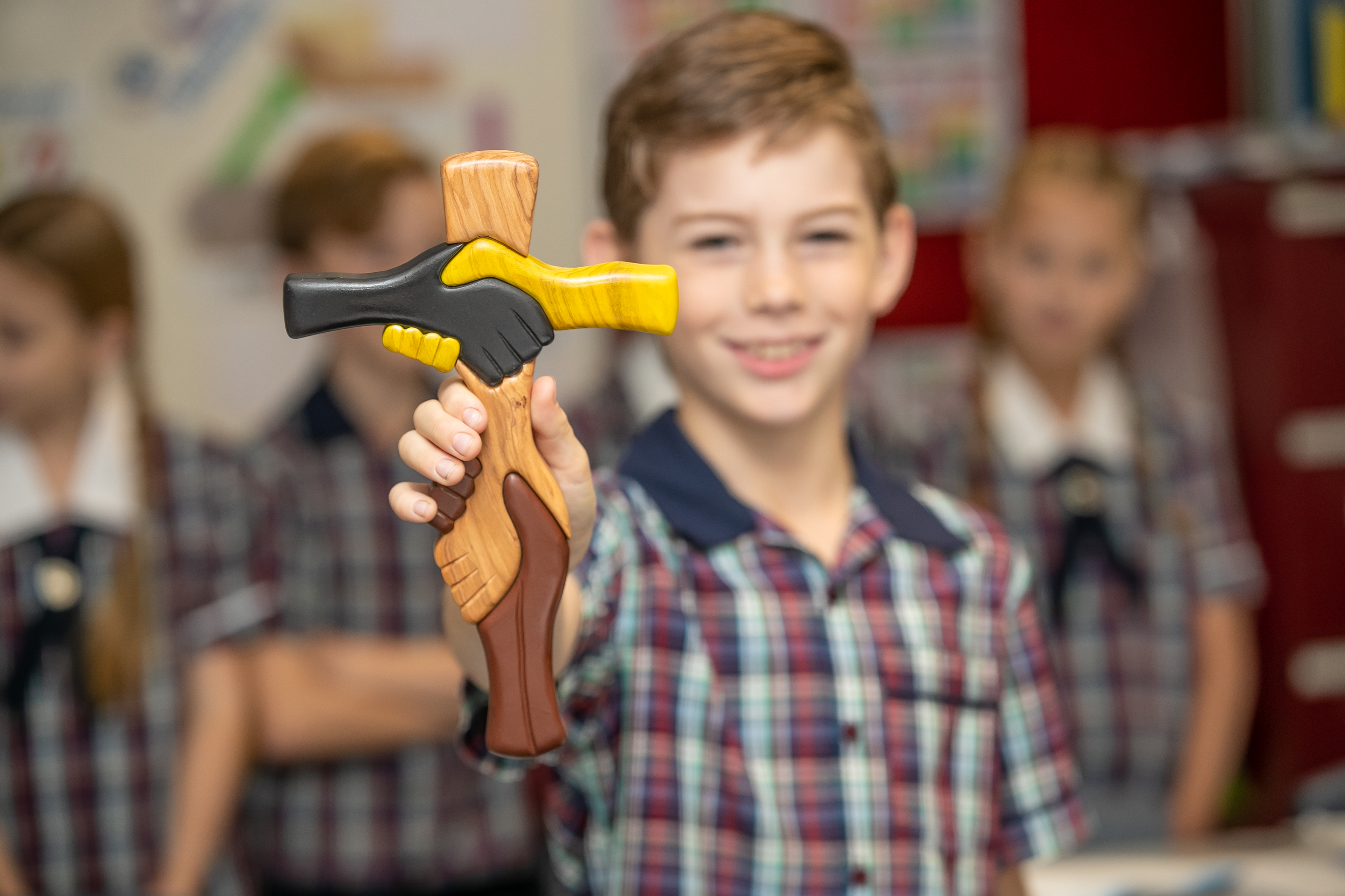 Student holding a cross featuring joined hands symbolising inclusion, respect and community in a classroom setting