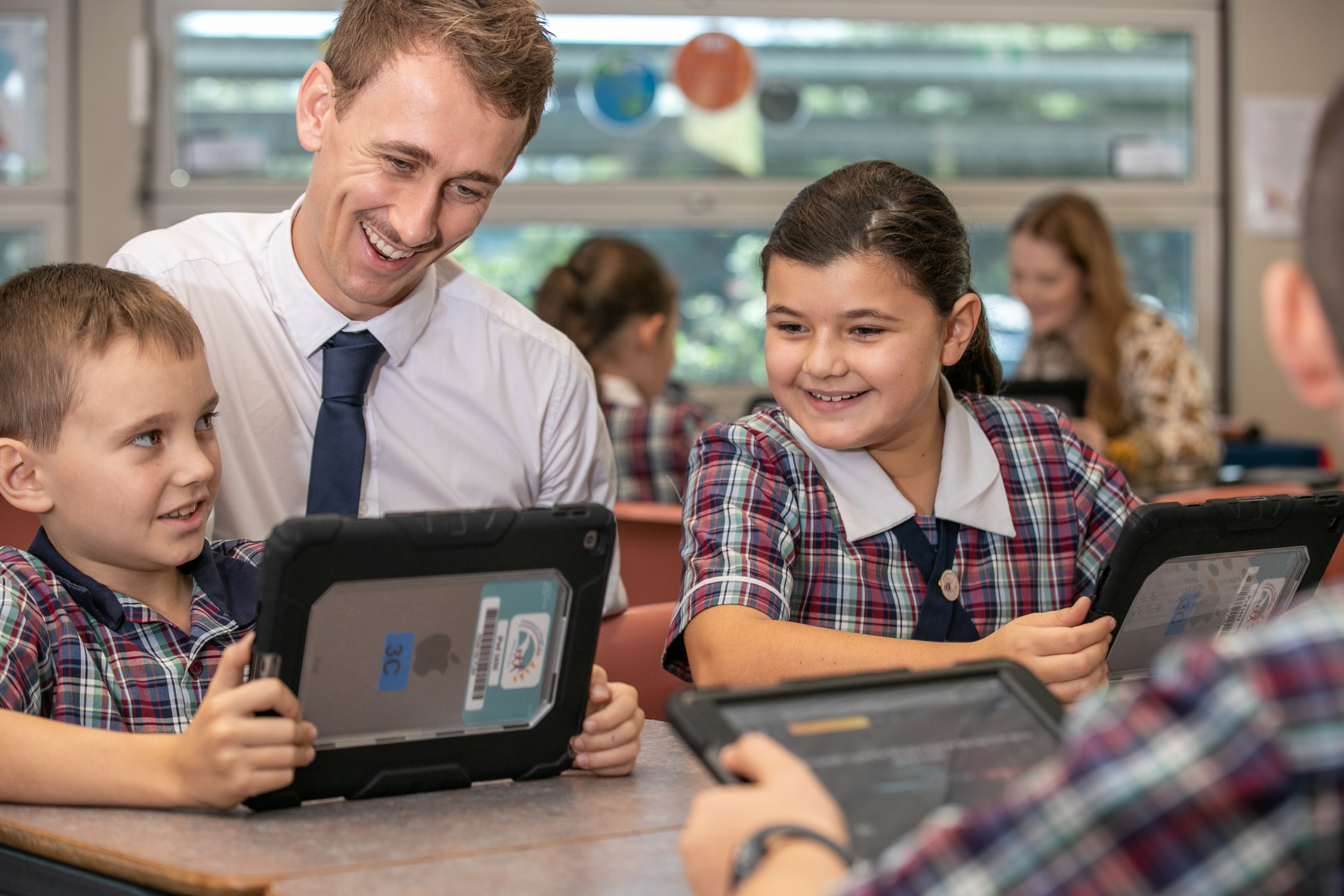 Teacher supporting a student using a tablet while other students learn in the classroom