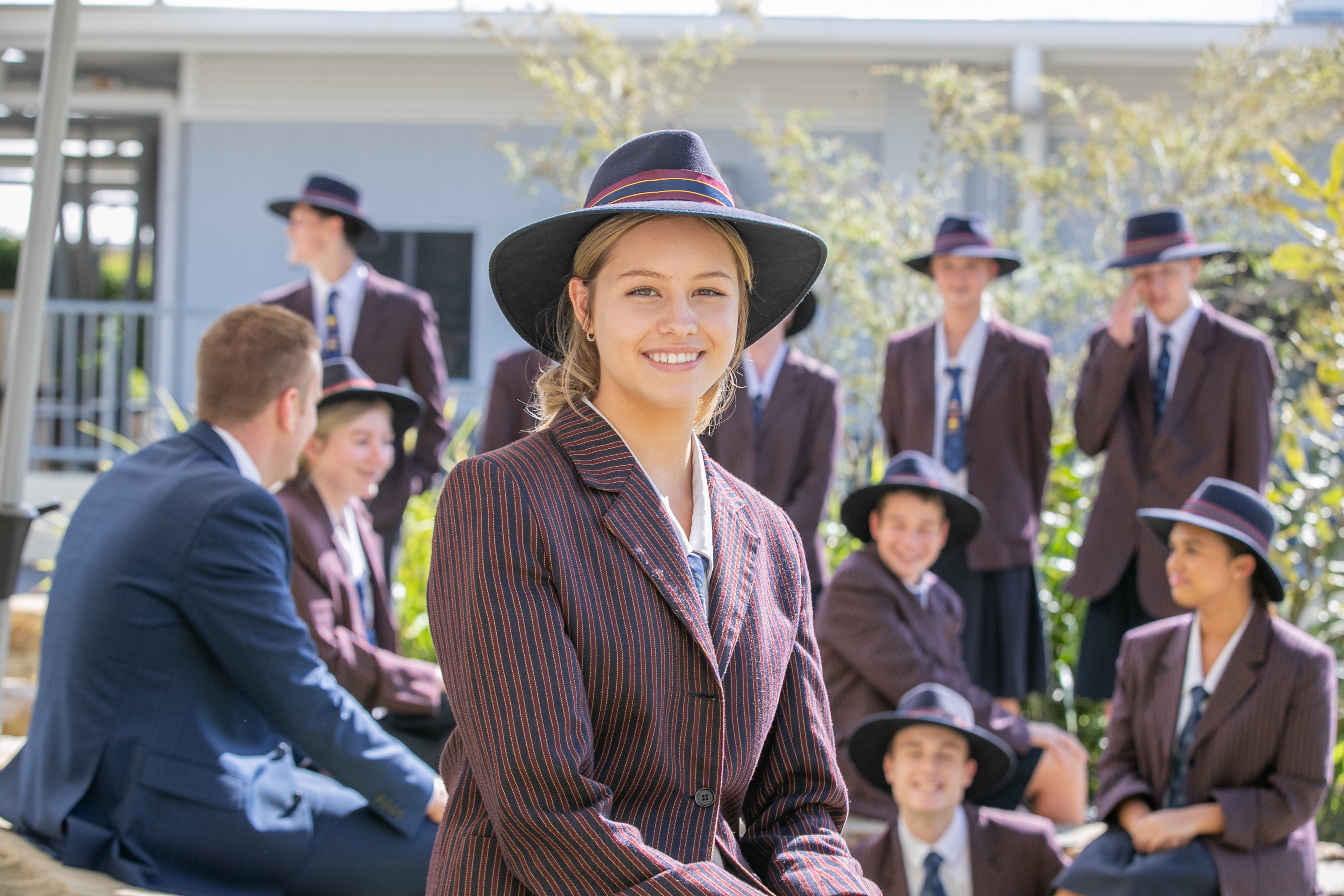 Secondary student in uniform standing outdoors with peers gathered in the background
