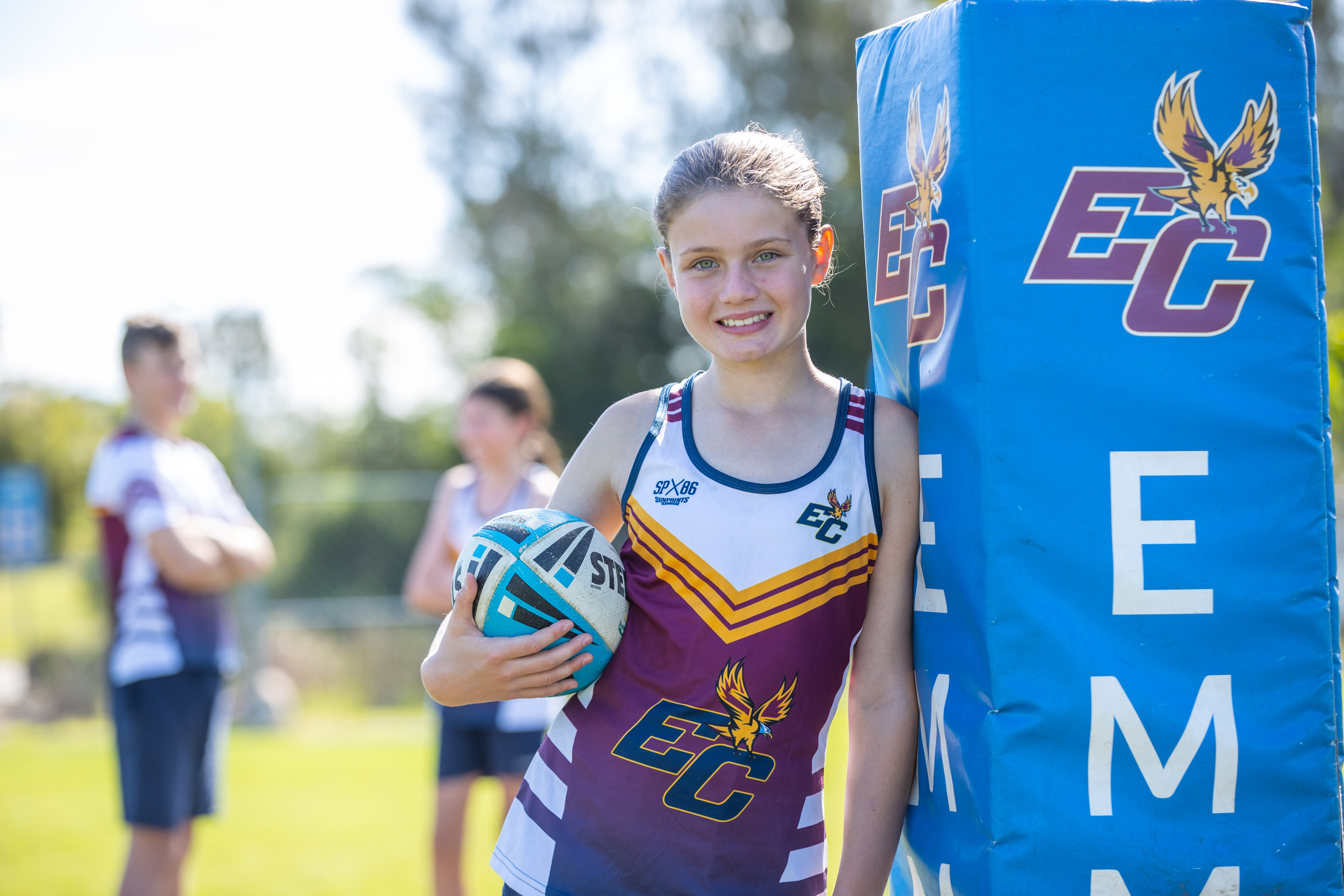 Student athlete holding a netball beside goal post on a school sports field