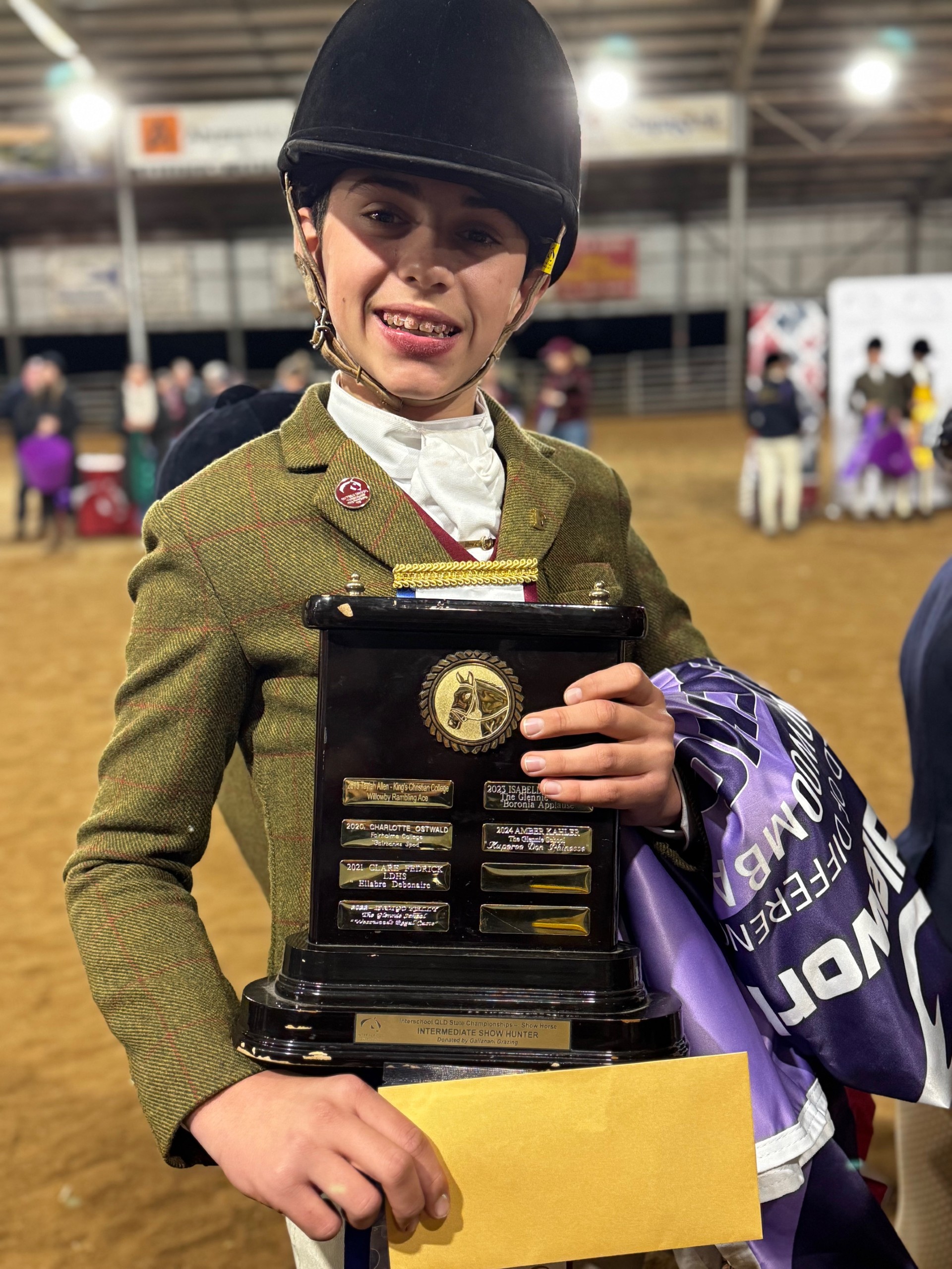 Student holding a championship trophy and award ribbon at an interschool equestrian event