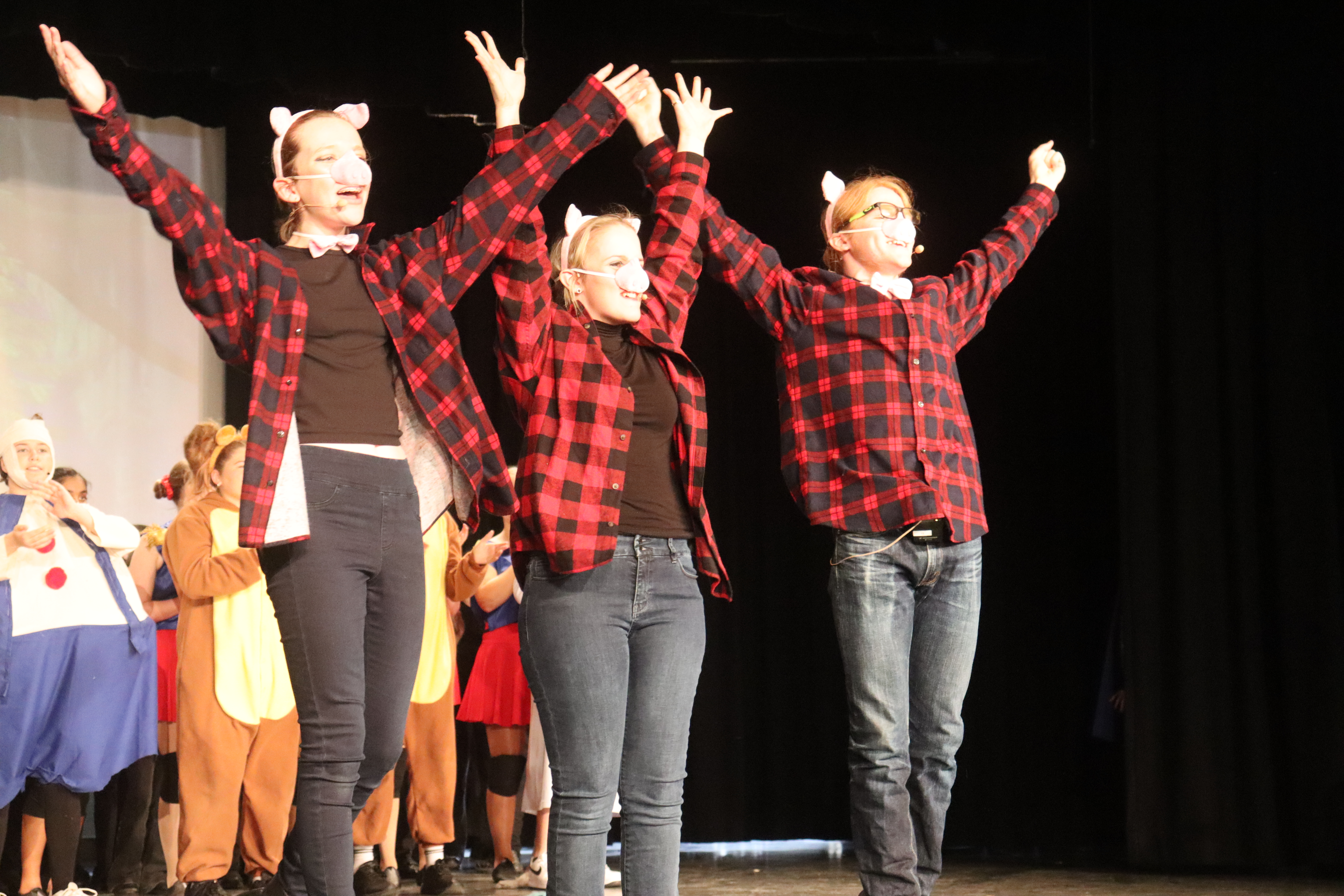 Three actors dressed as the Three Little Pigs cheering on stage at the end of the performance.