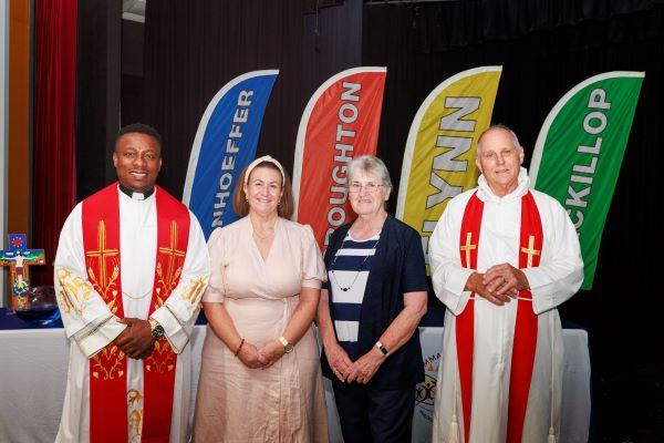 School clergy and staff standing together indoors in front of house banners during a school faith or community event